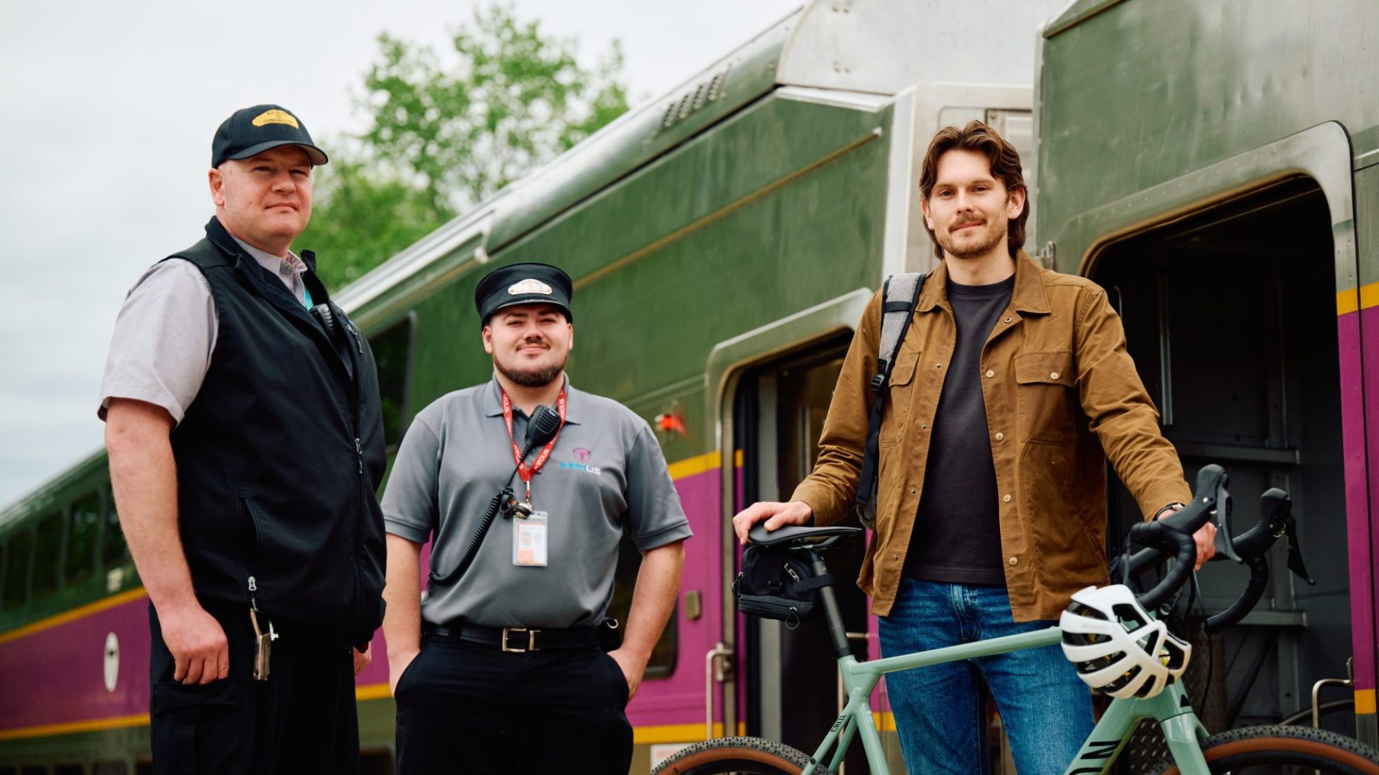 Commuter Rail passenger with bike poses for photo with conductors outside of the train.