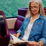 Woman with straight, silver hair reads a book on the train