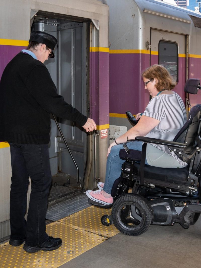 Woman in wheelchair boarding Commuter Rail train with assistance from conductor