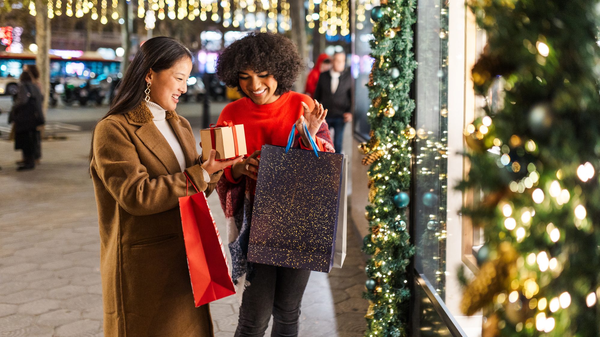 Two young women are having fun while going christmas shopping at night in a decorated city