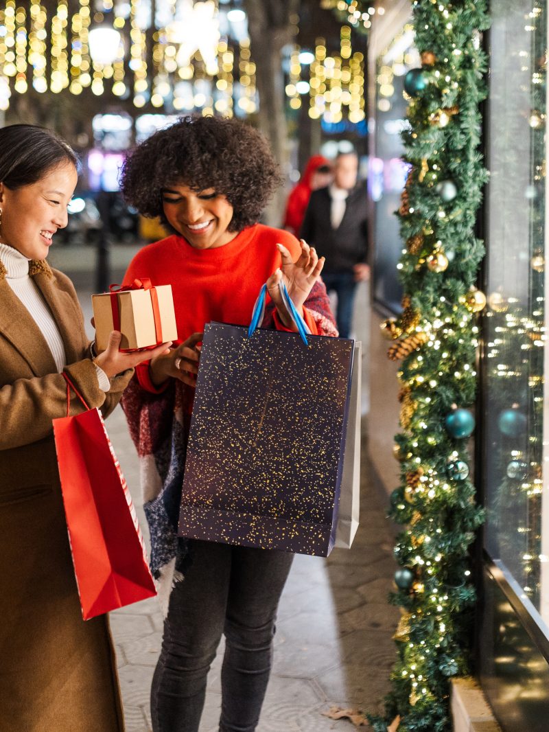 Two young women are having fun while going christmas shopping at night in a decorated city