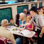 Train conductor interacts with family sitting at a table on a train.
