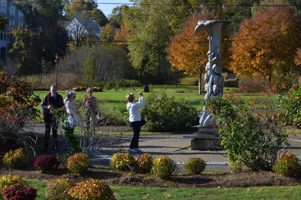Visitors to Plymouth during the fall take a photo of an outdoor statue in a garden.