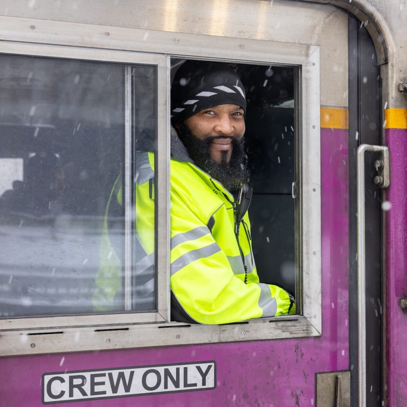 Train engineer smiling at the camera on a snowy day from inside the train.